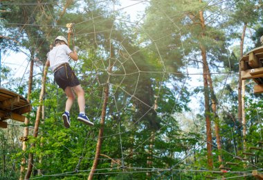 şirin, sportif çocuk kask ve güvenlik ekipmanları ile macera ip etkinlik parkta Beyaz tişörtlü. Genç çocuk oynamaya ve sahip eğlenceli aktiviteler açık havada yaptığını. Hobi, aktif yaşam tarzı kavramı