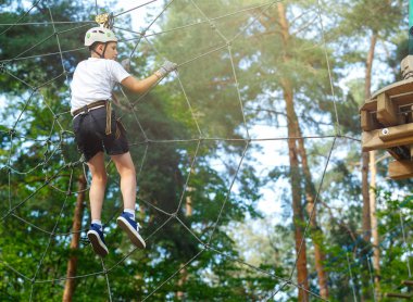 şirin, sportif çocuk kask ve güvenlik ekipmanları ile macera ip etkinlik parkta Beyaz tişörtlü. Genç çocuk oynamaya ve sahip eğlenceli aktiviteler açık havada yaptığını. Hobi, aktif yaşam tarzı kavramı