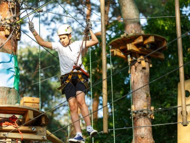 şirin, sportif çocuk kask ve güvenlik ekipmanları ile macera ip etkinlik parkta Beyaz tişörtlü. Genç çocuk oynamaya ve sahip eğlenceli aktiviteler açık havada yaptığını. Hobi, aktif yaşam tarzı kavramı