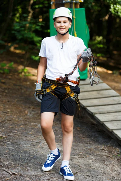 cute, sporty boy in white t shirt in the adventure rope activity park with helmet and safety equipment.Young boy playing and having fun doing activities outdoors. Hobby, active lifestyle concept
