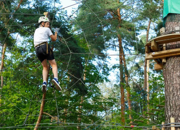 şirin, sportif çocuk kask ve güvenlik ekipmanları ile macera ip etkinlik parkta Beyaz tişörtlü. Genç çocuk oynamaya ve sahip eğlenceli aktiviteler açık havada yaptığını. Hobi, aktif yaşam tarzı kavramı