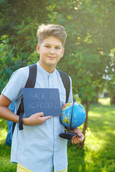 可爱的小男孩穿着蓝色衬衣在夏天在公园里抱着一个地球仪和空黑板 回到学校 教育理念 — 图库照片