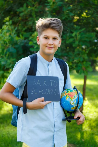 可爱的小男孩穿着蓝色衬衣在夏天在公园里抱着一个地球仪和空黑板 回到学校 教育理念 — 图库照片