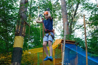 Eğleniyor ve Macera Parkı'nda oynarken, ipleri tutan ve ahşap merdiven çıkma mavi t gömlek ve turuncu kask mutlu, Sevimli, Genç çocuk. aktif yaşam tarzı kavramı