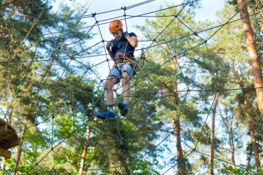 Eğleniyor ve Macera Parkı'nda oynarken, ipleri tutan ve ahşap merdiven çıkma mavi t gömlek ve turuncu kask mutlu, Sevimli, Genç çocuk. aktif yaşam tarzı kavramı