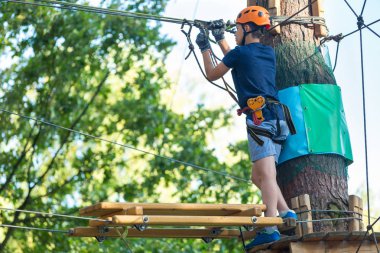 Eğleniyor ve Macera Parkı'nda oynarken, ipleri tutan ve ahşap merdiven çıkma mavi t gömlek ve turuncu kask mutlu, Sevimli, Genç çocuk. aktif yaşam tarzı kavramı