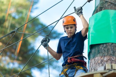 Mavi t gömlek ve eğleniyor ve Macera Parkı'nda oynarken, ipleri tutan ve ahşap merdiven çıkma kask mutlu, Sevimli, Genç çocuk. aktif yaşam tarzı kavramı