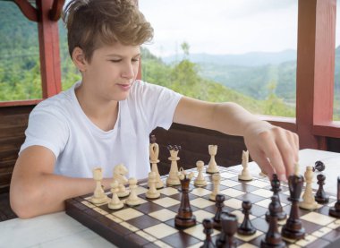 Beyaz tshirt şirin, zeki, yakışıklı çocuk yaz arbor dağ arka plan ile satranç oynar. Eğitim kavramı, entelektüel oyunu. Satranç dersi, eğitim kavramı