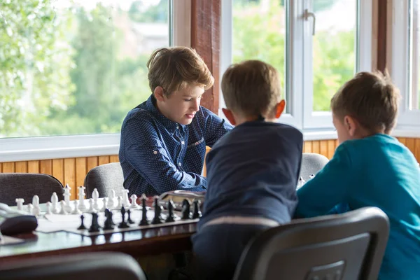 cute, smart boy in blue shirt sits in the classroom and plays chess on the chessboard. Training, lesson, hobby, education concept. intellectual game