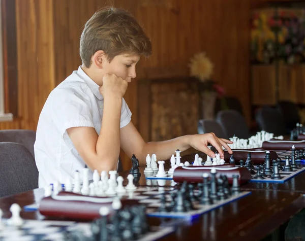 cute, smart, 11 years old boy in white shirt sits in the classroom and plays chess on the chessboard. Training, lesson, hobby, education concept. intellectual game.