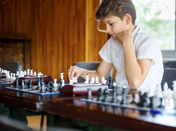 cute, smart, 11 years old boy in white shirt sits in the classroom and plays chess on the chessboard. Training, lesson, hobby, education concept. intellectual game.