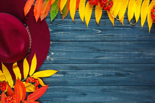 Burgundy  or marsala color hat on a gray wooden background with autumn yellow, red leaves and berries. Flat lay, copyspace