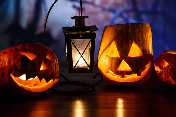 orange pumpkins with scary faces and candles lies on the table in front of dark blue background. Halloween celebration concept