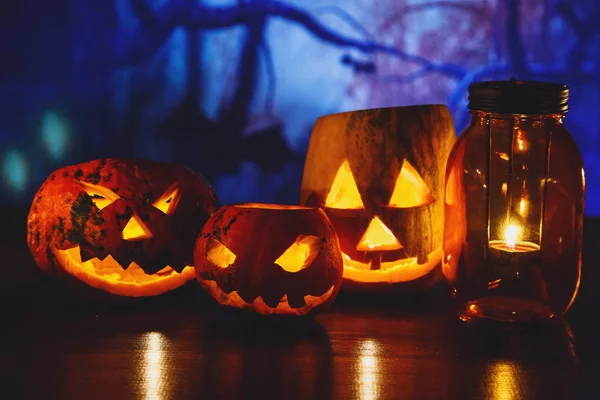 orange pumpkins with scary faces and candles lies on the table in front of dark blue background. Halloween celebration concept