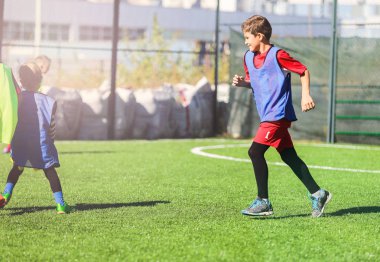 kırmızı ve mavi üniformalı genç yakışıklı yeşil çimenlerin üzerinde ekibiyle futbol oynar. Takım oyunu, eğitim, aktif yaşam tarzı, hobi, spor çocuklar konsepti için