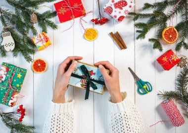 kadının ellerini Noel ve yeni yıl için el yapımı hediye, tablonun diğer hediyeleri arasında merkezinde beyaz arka plan üzerinde tutun. Alışveriş, Noel ve yeni yıl kutlama kavramı. üstten görünüm 