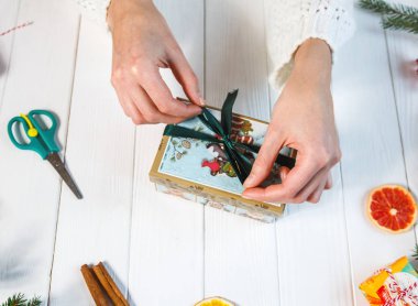 kadının ellerini Noel ve yeni yıl için el yapımı hediye, tablonun diğer hediyeleri arasında merkezinde beyaz arka plan üzerinde tutun. Alışveriş, Noel ve yeni yıl kutlama kavramı. üstten görünüm 