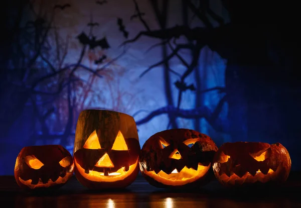 orange pumpkins with scary faces and candles lies on the table in front of dark blue background. Halloween celebration concept