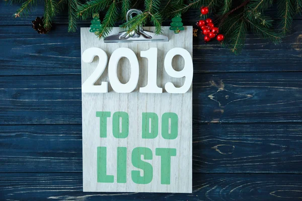 To do list  on wooden pad, white numbers 2019  and branches of fir tree, decor on grey wooden table. New Year  Goals list, things to do on Christmas concept. flat lay with copyspace.