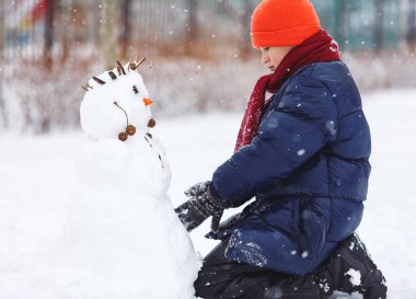 Güzel çocuk sıcak mavi ceketli, kırmızı şapka bir kardan adam kış günü yapar. Kış aktiviteleri, eğlenceli