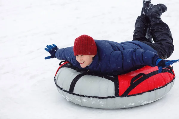 Child in blue jacket and red hat having fun on snow tube. Boy is riding a tubing. Winter entertainment, activities. active sport, lifestyle