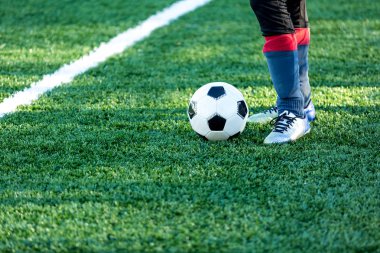 Klasik siyah ve beyaz futbol topu alan ve spor ayakkabılarla bacağından yeşil çimenlerin üzerinde. Eğitim, maç, hobi kavramı. kopya alanı ile 