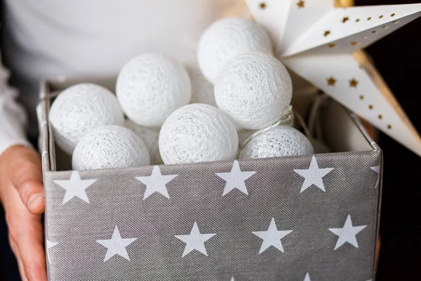 White cotton ball light garland in a grey basket on boys hands with stars sparkling at home. close up, bright lights, festive atmosphere. home decoration. New year and Christmas celebration concept