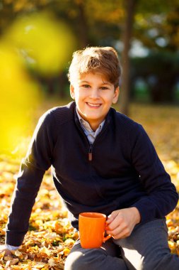 Çocuk turuncu fincan düşen yapraklar arka plan üzerinde elinde tutar. Sonbahar ruh hali güzel bir gün. Natürmort altın sonbaharda. Parlak sonbahar resim.  