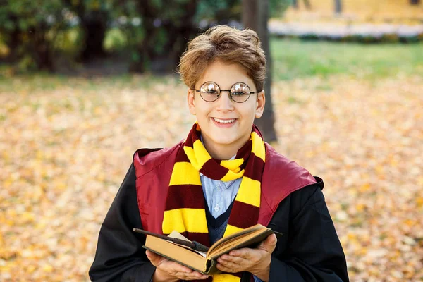 gözlüklü çocuk sonbahar parkta duruyor, değnek elinde tutar, kitap, siyah takım elbise ve çizgili eşarp takıyor. Cadılar Bayramı Kostüm, cosplay