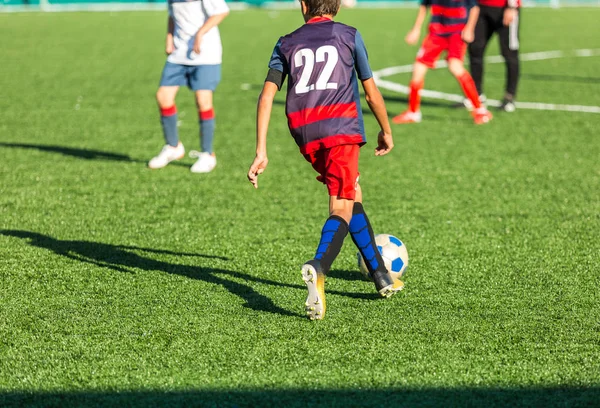 Junior football match. Boys in blue and white sportswear playing soccer match. Football stadium and grassy field in the background