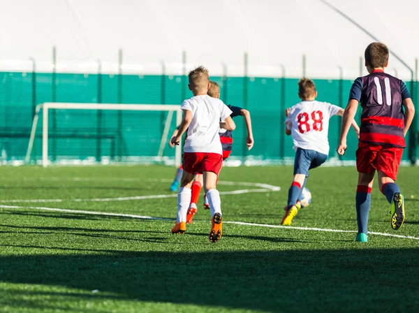 Junior football match. Boys in blue and white sportswear playing soccer match. Football stadium and grassy field in the background