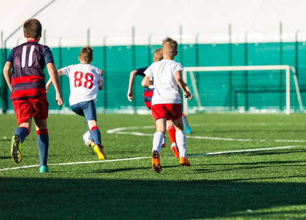 Junior football match. Boys in blue and white sportswear playing soccer match. Football stadium and grassy field in the background