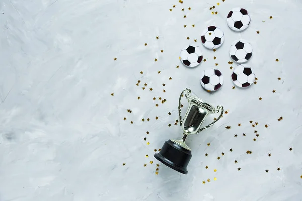 Golden trophy, confetti and black and white balls on gray cement background. sport achievement, football success concept. Gold trophy as a leader.