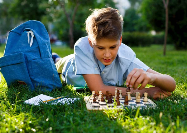 穿着蓝色衬衫的可爱男孩坐在公园的草地上 在木制棋盘上下棋 智力游戏理念 — 图库照片