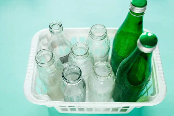 different glass bottle wastes ready for recycling in white basket on green background. Social responsibility, ecology care, recycling at home concept
