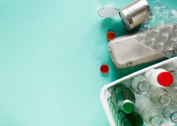 различные отходы готовы к переработке в белой корзине на зеленом фоне. Пластиковые бутылки, стекло, поднос для яиц. Социальная ответственность, уход за окружающей средой, переработка на дому концепции
