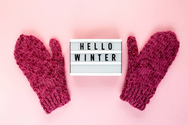 Warm, cozy winter mittens lightbox on pastel pink background. Christmas concept flat lay. Stylish winter clothes. Hello winter title