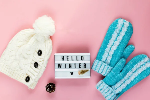 Warm, cozy winter clothing, mittens lightbox on pastel pink background. Christmas concept flat lay. Stylish winter clothes. Hello winter title