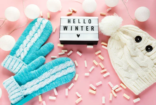 Warm, cozy winter clothing, mittens lightbox on pastel pink background. Christmas concept flat lay. Stylish winter clothes. Hello winter title