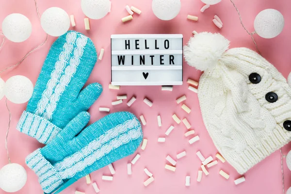 Warm, cozy winter clothing, mittens lightbox on pastel pink background. Christmas concept flat lay. Stylish winter clothes. Hello winter title