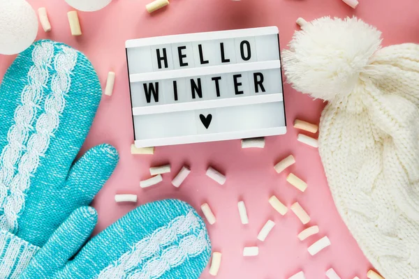 Warm, cozy winter clothing, mittens lightbox on pastel pink background. Christmas concept flat lay. Stylish winter clothes. Hello winter title