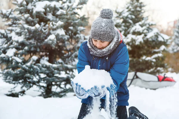 cute young boy in red hat blue jacket holds and plays with snow, has fun, smiles, makes snowman in winter park. Active lifestyle, winter activity, outdoor winter games, snowballs.