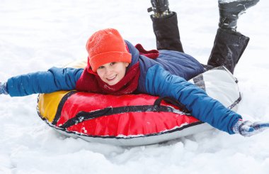 sevimli genç çocuk şapka kırmızı eşarp ve mavi ceketli kar tüp üzerinde bırakır, eğlenir, gülümsüyor. Genç ellerini kış parkta yükselir. Aktif yaşam tarzı, Kış etkinliği, Açık Kış oyunları, kartopu