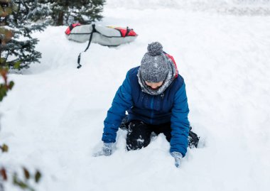 sevimli genç çocuk turuncu şapka mavi ceketli kar ile oynar, eğlenir, gülümsüyor. Genç kardan adam kış parkta yapar. Aktif yaşam tarzı, Kış etkinliği, Açık Kış oyunları, kartopu. 