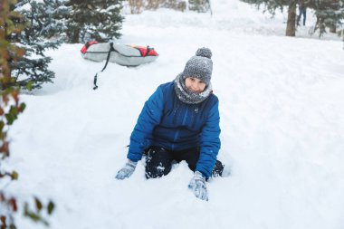 sevimli genç çocuk turuncu şapka mavi ceketli kar ile oynar, eğlenir, gülümsüyor. Genç kardan adam kış parkta yapar. Aktif yaşam tarzı, Kış etkinliği, Açık Kış oyunları, kartopu. 