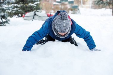 sevimli genç çocuk turuncu şapka mavi ceketli kar ile oynar, eğlenir, gülümsüyor. Genç kardan adam kış parkta yapar. Aktif yaşam tarzı, Kış etkinliği, Açık Kış oyunları, kartopu. 