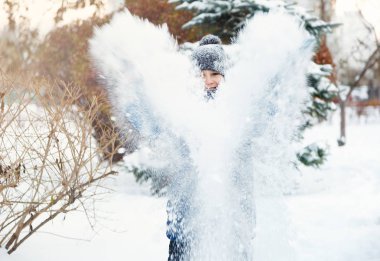 sevimli genç çocuk turuncu şapka mavi ceketli kar ile oynar, eğlenir, gülümsüyor. Genç ellerini kış parkta yükselir. Aktif yaşam tarzı, Kış etkinliği, Açık Kış oyunları, kartopu. bulanık kar