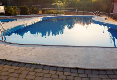 Modern yüzme havuzu görünümünü günbatımında otel kapatın. Yüzeyde güneş ışığı. Yaz tatili, tatil, sakin ol, yaz etkinlikleri kavramı