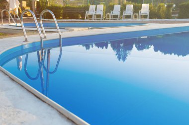 Modern yüzme havuzu görünümünü günbatımında otel kapatın. Yüzeyde güneş ışığı. Yaz tatili, tatil, sakin ol, yaz etkinlikleri kavramı