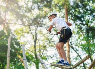 Orman macera parkı çocuk. Çocuk beyaz kask ve beyaz t gömlek tırmanıyor yüksek ip izinde. Çeviklik beceri ve açık hava eğlence merkezi çocuklar için tırmanma. Genç çocuk açık havada çalış